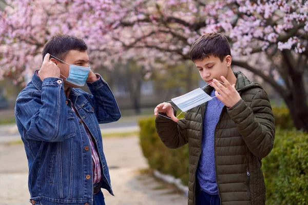 顔のマスクを持つ父と息子は街の屋外にあり 木を咲かせ 春の季節 開花期 アレルギーとほこりの多い空気からの健康保護の概念 — ストック写真