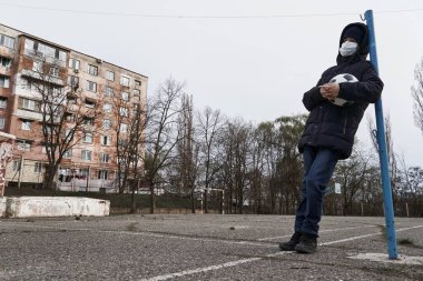 Salgın ve karantina kavramı. Yüzü maskeli bir çocuk ve şehirde tek başına bir top.
