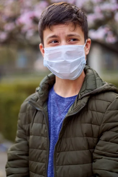 顔のマスクを持つ男の子は街の屋外にあり 木を咲かせ 春の季節 開花時間 ほこりの多い空気からのアレルギーと健康保護の概念 — ストック写真