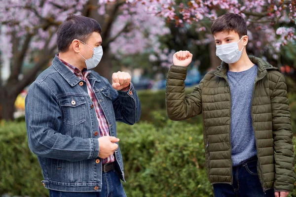 顔のマスクを持つ父と息子は 街の屋外で手を振る 木を咲かせ 春の季節 開花時間 アレルギーとほこりの多い空気からの健康保護の概念 — ストック写真