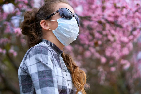 フェイスマスクを持つ女の子は街の屋外にあり 木を咲かせ 春の季節 開花時間 ほこりの多い空気からのアレルギーと健康保護の概念 — ストック写真