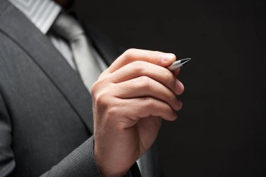 Bir kalem yakın plan iş adamı eli, gri takım elbise, koyu duvar arkaplan