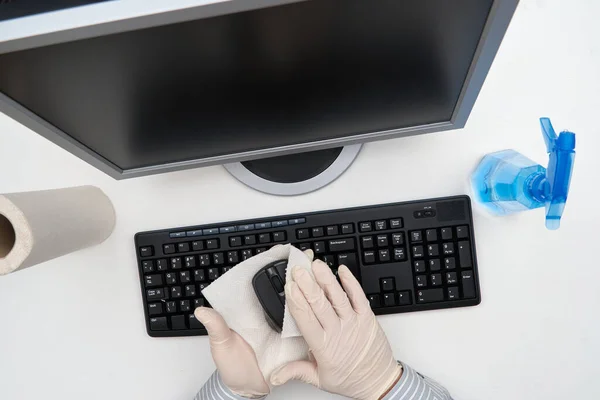 concept of cleaning or disinfecting the office - a businessman cleans the workplace, computer, desk, uses a spray gun and paper napkins. Cleaning surfaces from microbes, viruses and dirt.