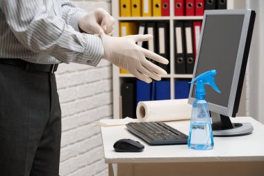 Ofisi temizleme ya da dezenfekte etme kavramı - bir işadamı iş yerini, bilgisayarı, masayı temizler, sprey tabanca ve kağıt peçete kullanır. Mikropların, virüslerin ve toprağın temiz yüzeyleri.