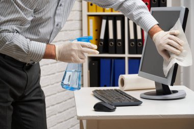 Ofisi temizleme ya da dezenfekte etme kavramı - bir işadamı iş yerini, bilgisayarı, masayı temizler, sprey tabanca ve kağıt peçete kullanır. Mikropların, virüslerin ve toprağın temiz yüzeyleri.