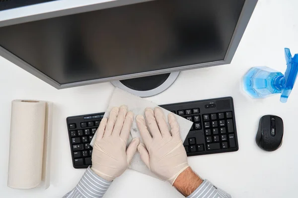 concept of cleaning or disinfecting the office - a businessman cleans the workplace, computer, desk, uses a spray gun and paper napkins. Cleaning surfaces from microbes, viruses and dirt.