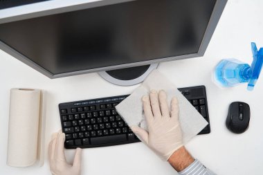 Ofisi temizleme ya da dezenfekte etme kavramı - bir işadamı iş yerini, bilgisayarı, masayı temizler, sprey tabanca ve kağıt peçete kullanır. Mikropların, virüslerin ve toprağın temiz yüzeyleri.