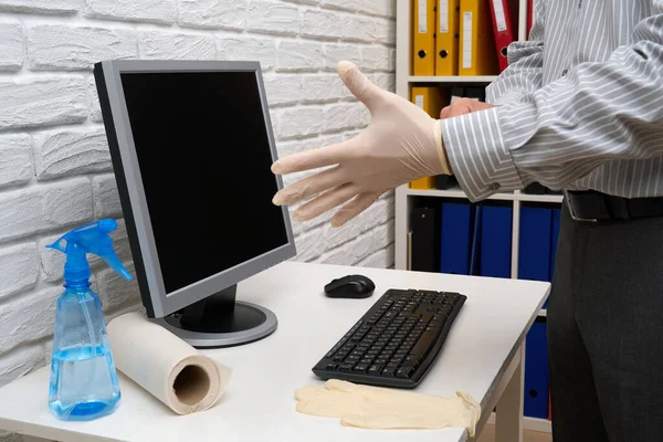 concept of cleaning or disinfecting the office - a businessman cleans the workplace, computer, desk, uses a spray gun and paper napkins. Cleaning surfaces from microbes, viruses and dirt.