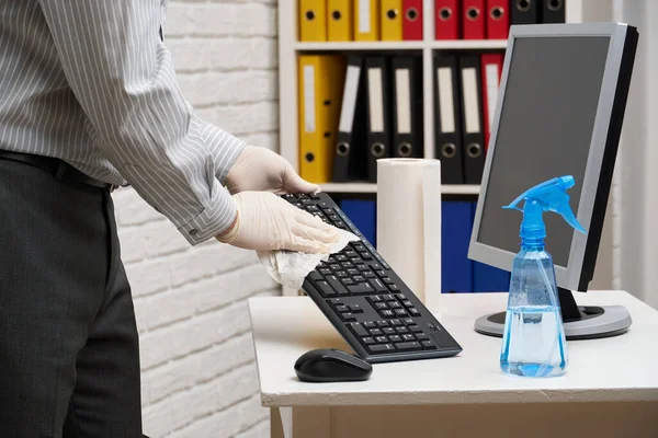 concept of cleaning or disinfecting the office - a businessman cleans the workplace, computer, desk, uses a spray gun and paper napkins. Cleaning surfaces from microbes, viruses and dirt.