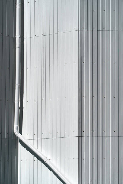 White metal siding on a wall and drain pipe as background