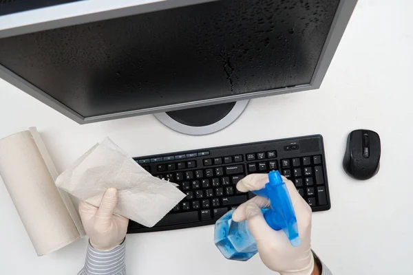 concept of cleaning or disinfecting the office - a businessman cleans the workplace, computer, desk, uses a spray gun and paper napkins. Cleaning surfaces from microbes, viruses and dirt.