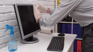 Ofisi temizleme ya da dezenfekte etme kavramı - bir işadamı iş yerini, bilgisayarı, masayı temizler, sprey tabanca ve kağıt peçete kullanır. Mikropların, virüslerin ve toprağın temiz yüzeyleri.