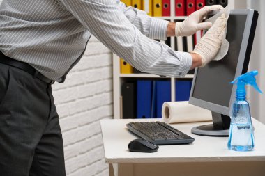 Ofisi temizleme ya da dezenfekte etme kavramı - bir işadamı iş yerini, bilgisayarı, masayı temizler, sprey tabanca ve kağıt peçete kullanır. Mikropların, virüslerin ve toprağın temiz yüzeyleri.