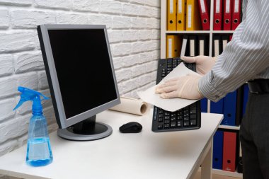 Ofisi temizleme ya da dezenfekte etme kavramı - bir işadamı iş yerini, bilgisayarı, masayı temizler, sprey tabanca ve kağıt peçete kullanır. Mikropların, virüslerin ve toprağın temiz yüzeyleri.