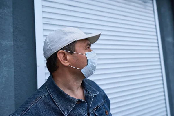 壁の近くにポーズをとって高層ビルのドアを閉めた男アパート住宅地顔の医療マスクはウイルスやほこりから身を守る — ストック写真