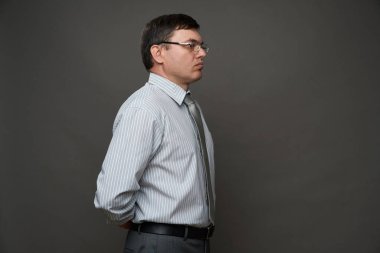 Stüdyoda gri arka planda poz veren, gözlüklü, açık renk çizgili gömlek ve kravat giyen bir iş adamı.