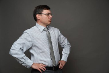 Stüdyoda gri arka planda poz veren, gözlüklü, açık renk çizgili gömlek ve kravat giyen bir iş adamı.