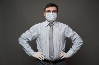 İş adamı gibi giyinmiş, stüdyoda gri arka planda poz veren, tıbbi maske ve koruyucu eldivenler, gözlük, gömlek ve kravat - karantina ve antivirüs koruması konsepti
