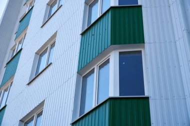 Beyaz ve yeşil metal kaplamalı çok katlı yeni bir binanın ön cephesi, birçok pencere