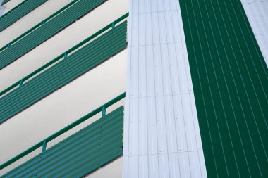 Beyaz ve yeşil metal kaplamalı çok katlı yeni bir binanın ön cephesi, birçok Windows
