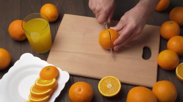 キッチンカットボード上のオレンジのスライス 背景として木製のテーブル 近いビュー オレンジジュースのグラス — ストック動画