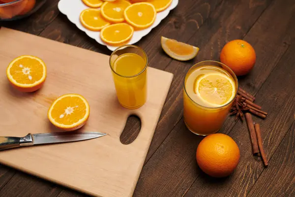 新鮮なオレンジフルーツ全体と木製のテーブルの上にスライス まな板とキッチンナイフ 柑橘類のスライスでいっぱいのプレート 自然と健康食品 フルーツカクテルのグラス — ストック写真