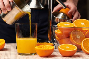 Bir portakalı elle sıkmak, yakın görüş, taze bir bardak yapmak. Tahta bir masada taze portakallar, sıkılmış ve dilimlenmiş..