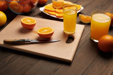 Taze portakal meyvesi ve ahşap bir masada dilimlenmiş tahta ve mutfak bıçağı. Turunçgil dilimleriyle dolu bir tabak. Doğal ve sağlıklı yiyecek. Bir bardak meyve kokteyli..