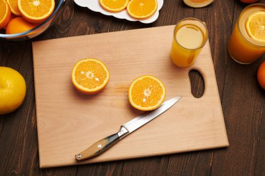 Taze portakal meyvesi ve ahşap bir masada dilimlenmiş tahta ve mutfak bıçağı. Turunçgil dilimleriyle dolu bir tabak. Doğal ve sağlıklı yiyecek. Bir bardak meyve kokteyli..