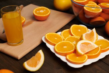 Taze portakal meyvesi ve ahşap bir masada dilimlenmiş tahta ve mutfak bıçağı. Turunçgil dilimleriyle dolu bir tabak. Doğal ve sağlıklı yiyecek. Bir bardak meyve kokteyli..