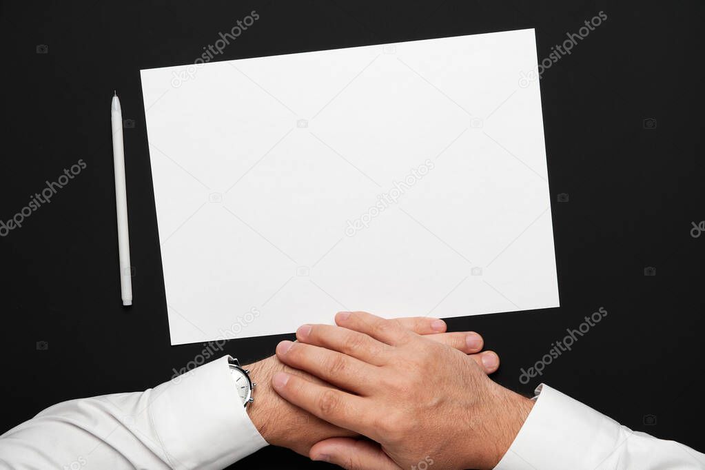 a blank sheet of paper and a businessman's hands on a black table, a white shirt and a wrist watch, a top view-a template for any text or inscription