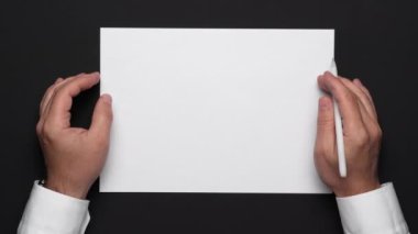 Boş bir kağıt parçası ve siyah bir masa, beyaz gömlek ve kol saati üzerinde bir iş adamının elleri.