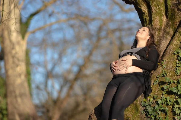 Mujer embarazada recostada sobre el árbol — Foto de Stock