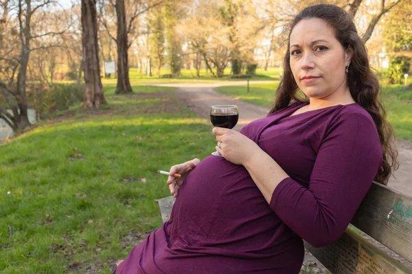 Pregnant woman with alcohol and cigarette in park — Stock Photo, Image