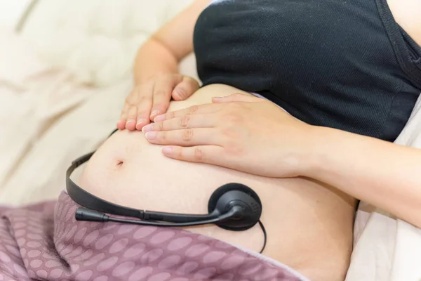 Mãos grávidas e fone de ouvido na barriga — Fotografia de Stock