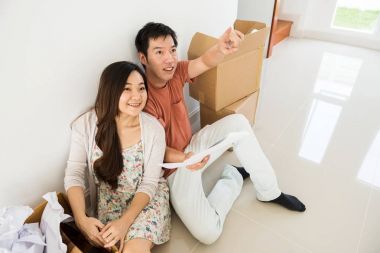 Asya Genç çift yeni boş ev planı. Bir plan ve mutlu gülümseme koca noktası parmak arzu planını dekorasyon duvar ve tavan için bakmak. İlk satın alma ev ile başlatmak için yeni bir hayat.