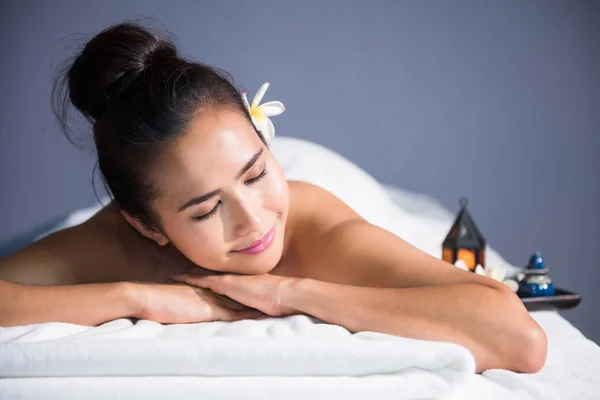 portrait of young happy Asian beautiful woman relax in spa. Body care treatment. Cute girl having massage at back by professional massager hands with candle and white Plumeria on bed.