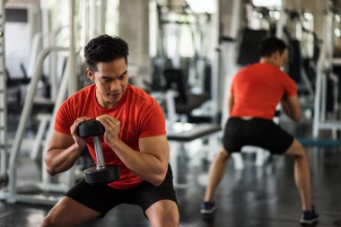 Erkek, spor salonunda halterin yanında biseps egzersizi yapar.