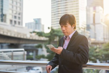 İş adamı ofis binasının dışında telefonla mesaj atıyor.