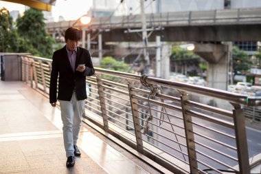 İş adamı şehirde telefonda yürüyüp mesaj atıyor.