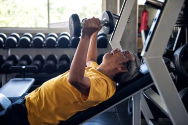 Yaşlı adam spor salonunda dambılları kaldırıyor.