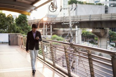 İş adamı gün batımında telefonda yürüyüp mesaj atıyor.