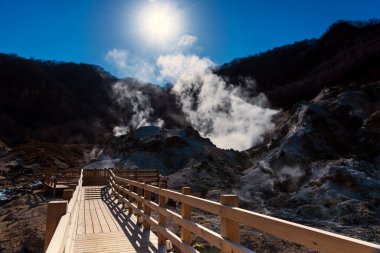 Jigokudani cehennem vadisi yürüyüş yolu ya da ahşap patika yolu sülfür sisli, mavi gökyüzü ve güneş ışığı Noboribetsu, Hokkaido, Japonya 'da. Kentte hamamlı ünlü doğal seyahat merkezi..