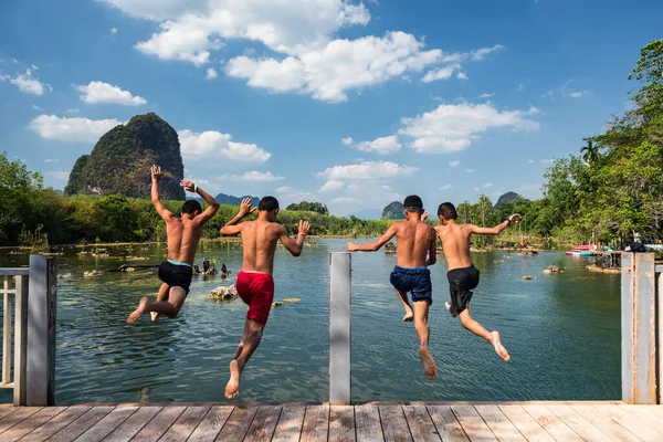 Rear happy childern boys jump tp water with blue sky and Limestone mountain background at Klong Rood, Krabi, Thailand. Famous travel destination to kayak and swim.