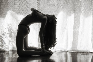 Çıplak üstsüz kadın yogası ya da pencerenin yanında egzersiz. Beyaz perdenin çiçek desenli ışığı olan çıplak sanat konsepti. Odada çekici bir kız var. Siyah ve beyaz renk süreci.