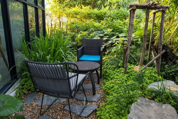 outdoor relax desk chair and table of coffee shop with spring natural graden before sunset. two chairs surrounded by green trees and leaves near house.