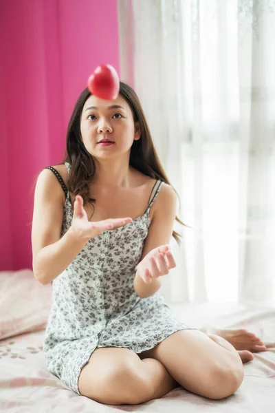 Lonely Attractive Asian beautiful woman on bed play with red heart due to stay safe at house to prevent covid-19 or coronavirus disease. Quarantine, work from home, social distancing.
