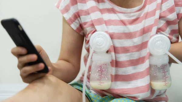 母亲在网上购物 用智能手机播放社交媒体时 用自动抽奶机给奶瓶抽奶 当妈的 — 图库照片