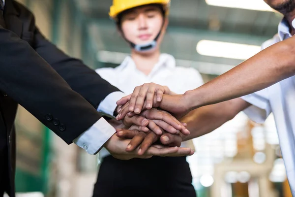 Stack hands together of factory owner or manager, female specialist, and old worker in factory. Synergy and teamwork concept to succeed heavy industry or business.