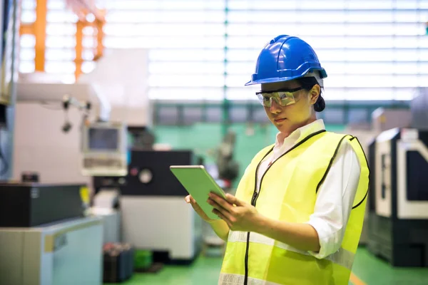 在工厂里 带着硬礼帽和防护眼镜的女工用公司的应用程序检查自动化机器人机器 用技术制造工业 Covid 19期间的社会疏离 图库图片